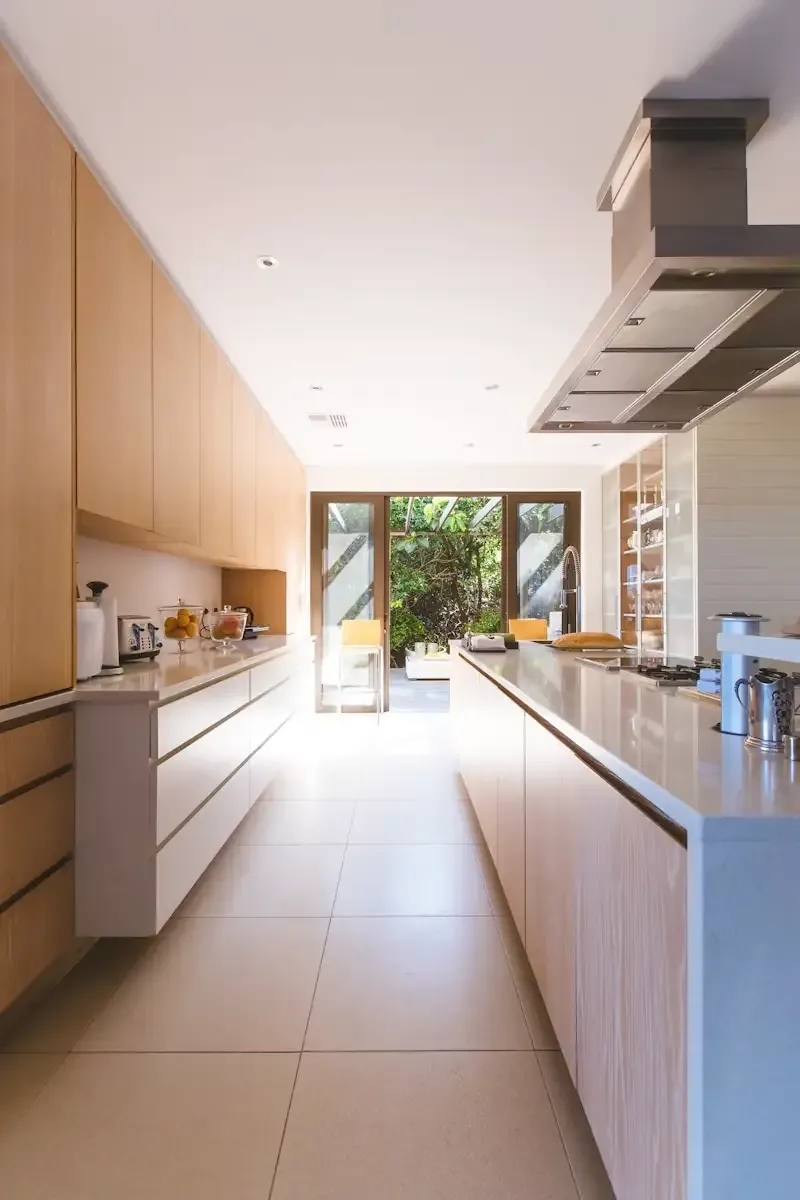 Galley kitchen with flat-panel oak cabinetry opening to an outdoor courtyard