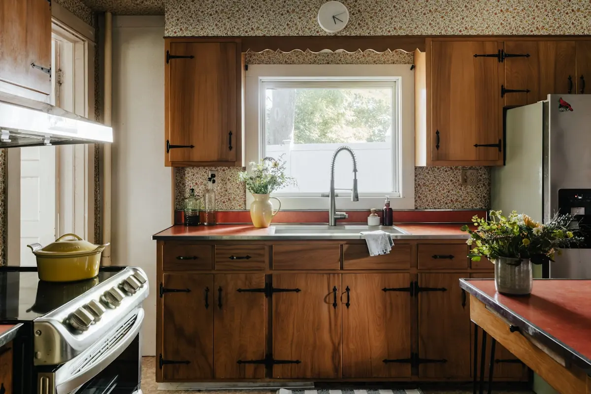Dated 1960s kitchen with dark wood cabinets and floral wallpaper before renovation