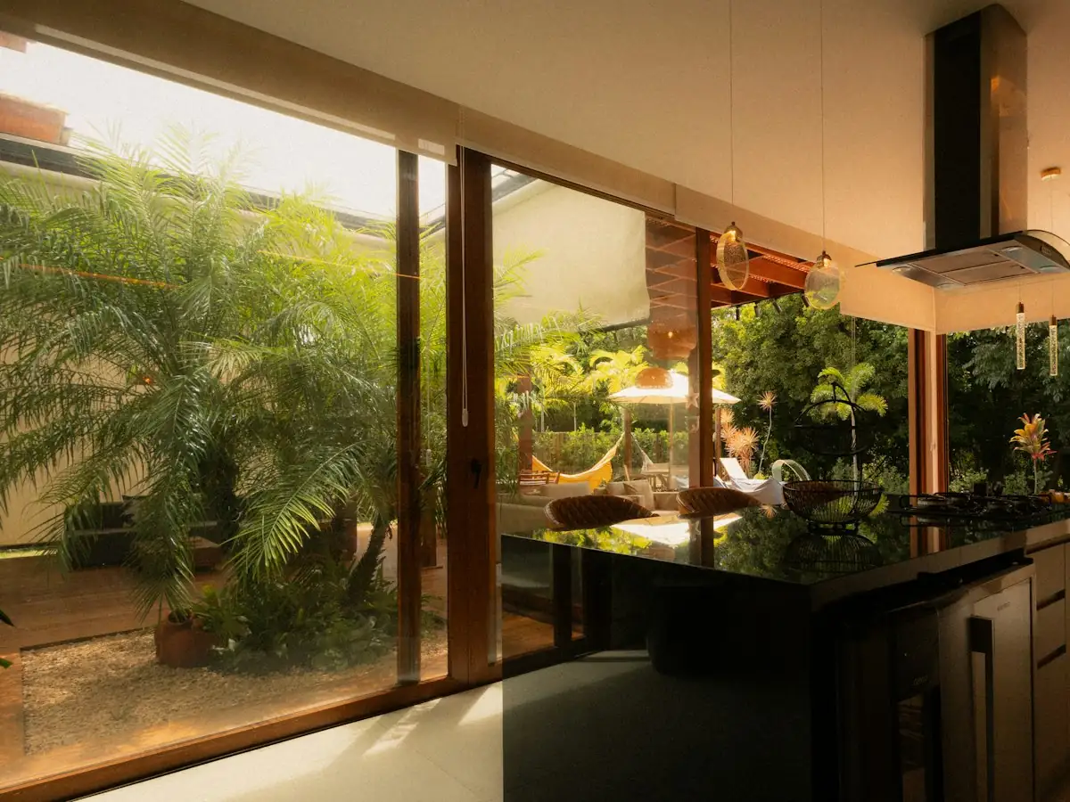 Kitchen island beside a floor-to-ceiling glass wall opening onto a landscaped garden, Eichler-style indoor-outdoor kitchen remodel