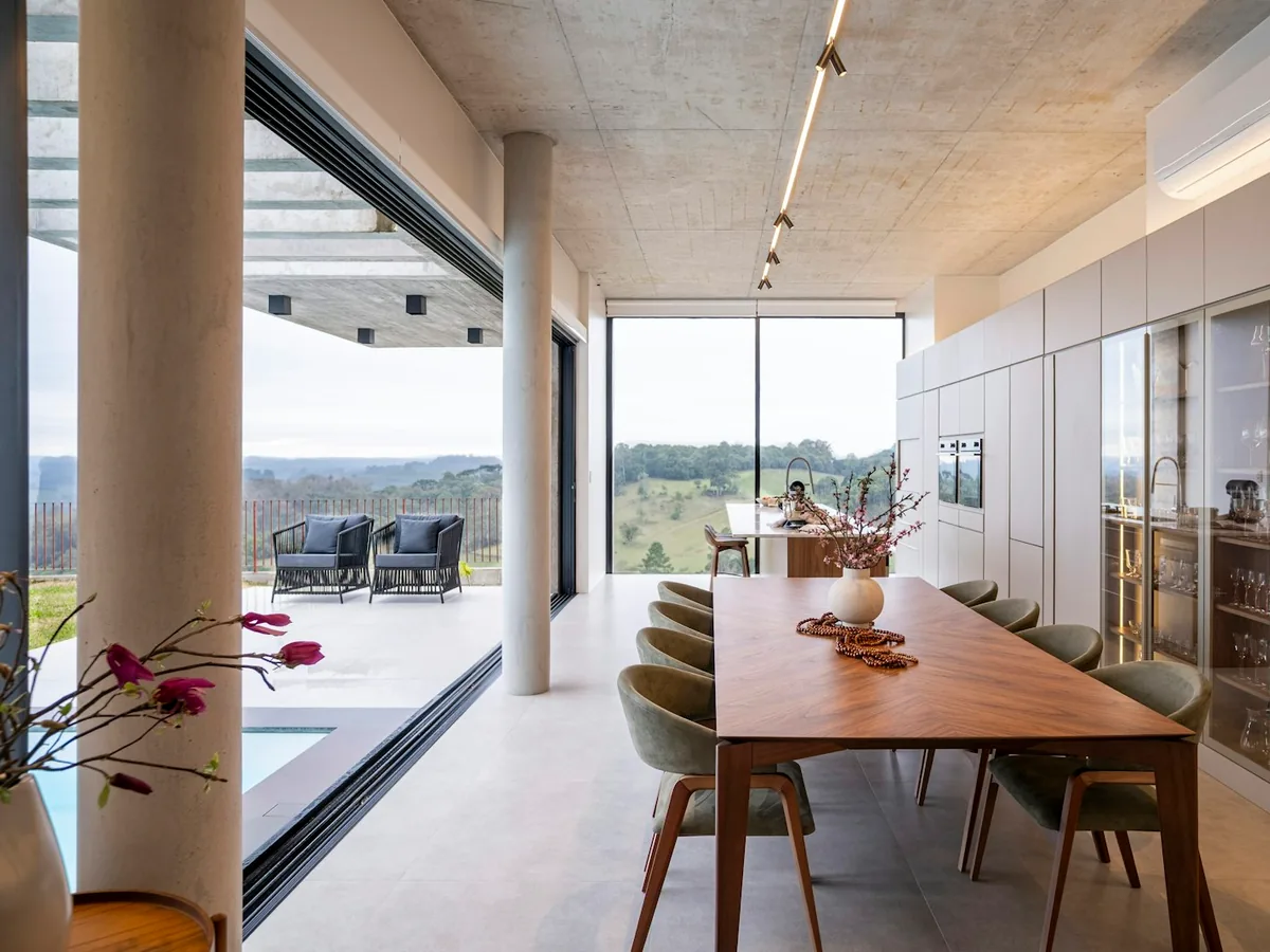 Open kitchen and dining area with floor-to-ceiling glass walls overlooking a hillside view, high-end structural kitchen remodel