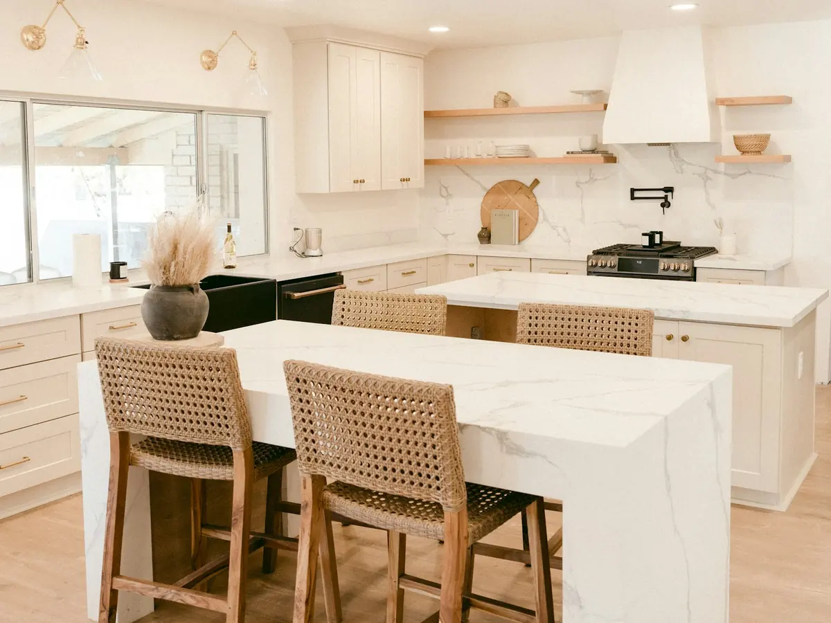 Traditional kitchen with a white marble waterfall island, woven counter stools, and open wood shelving