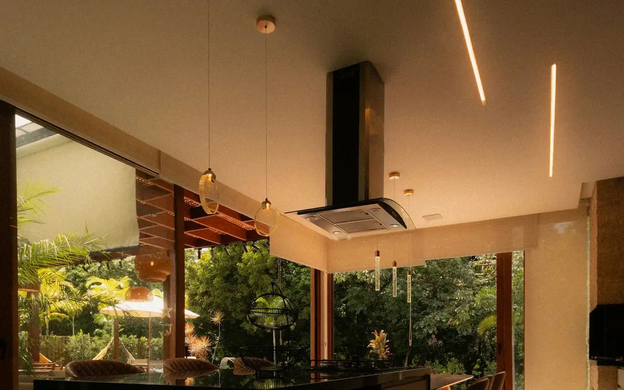 Kitchen island opening through glass walls to a lush backyard at dusk, with pendant lighting overhead