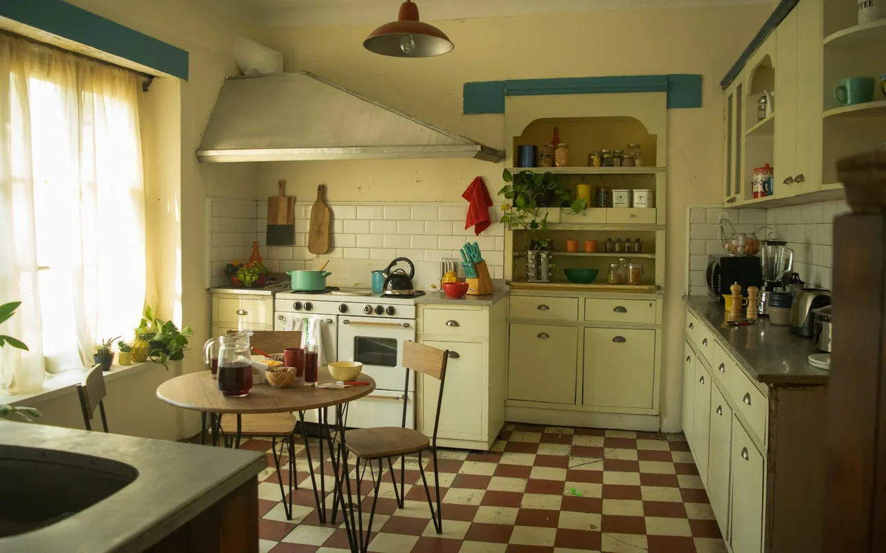Vintage cottage-style kitchen with cream cabinetry, checkered tile floor, and a breakfast table by the window