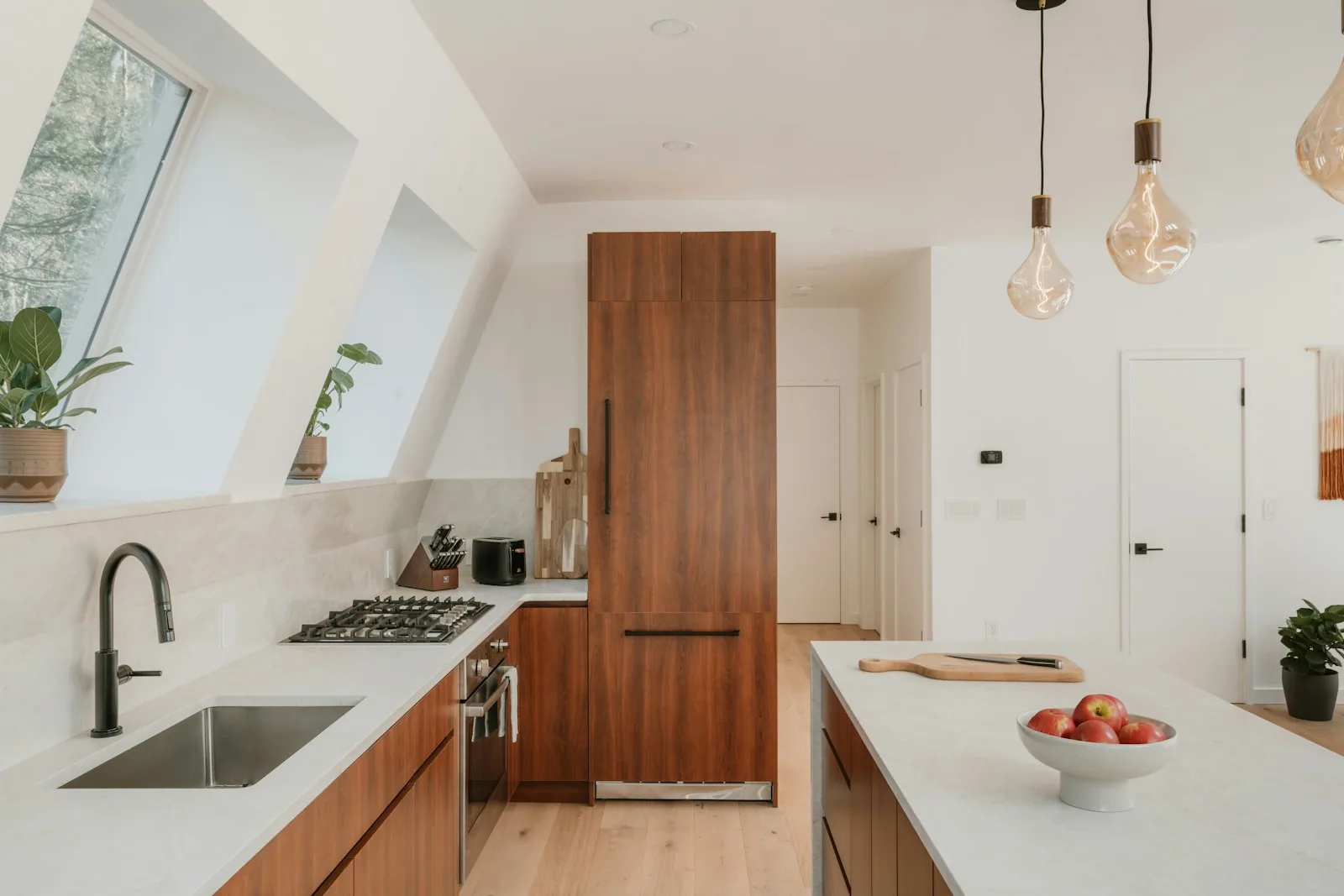 Kitchen with an angled ceiling and triangular windows, walnut cabinetry, and hanging bulb pendant lights
