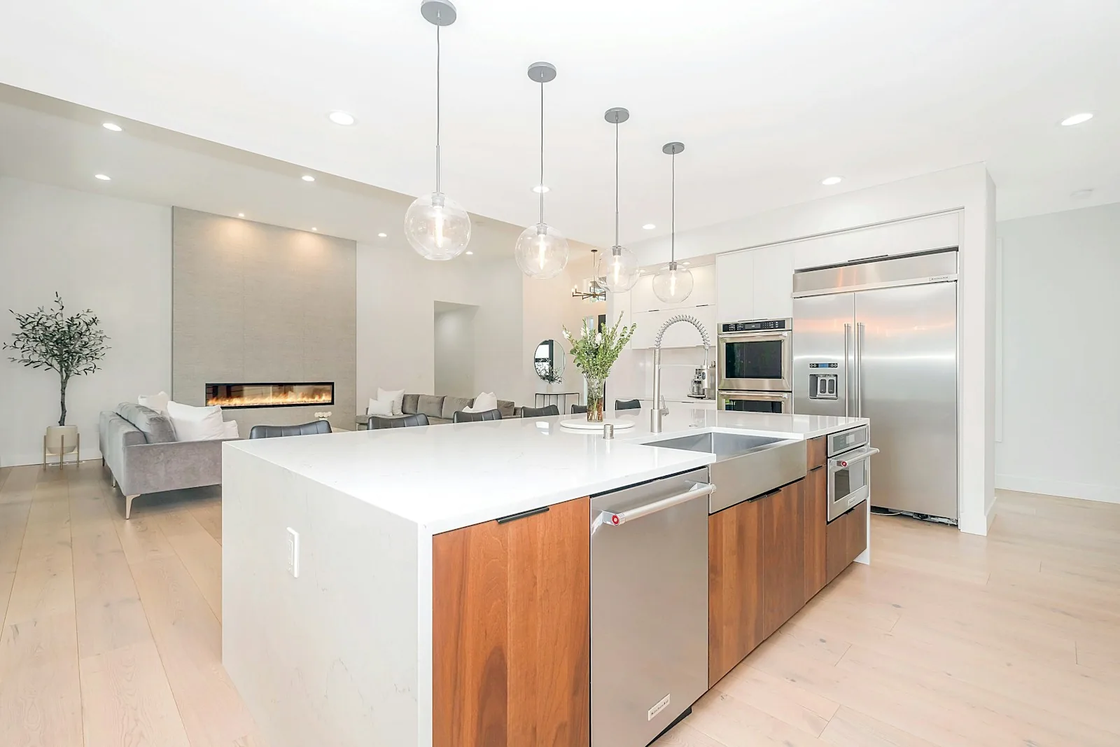 Open kitchen with walnut island cabinetry, white quartz waterfall countertop, and globe pendant lighting